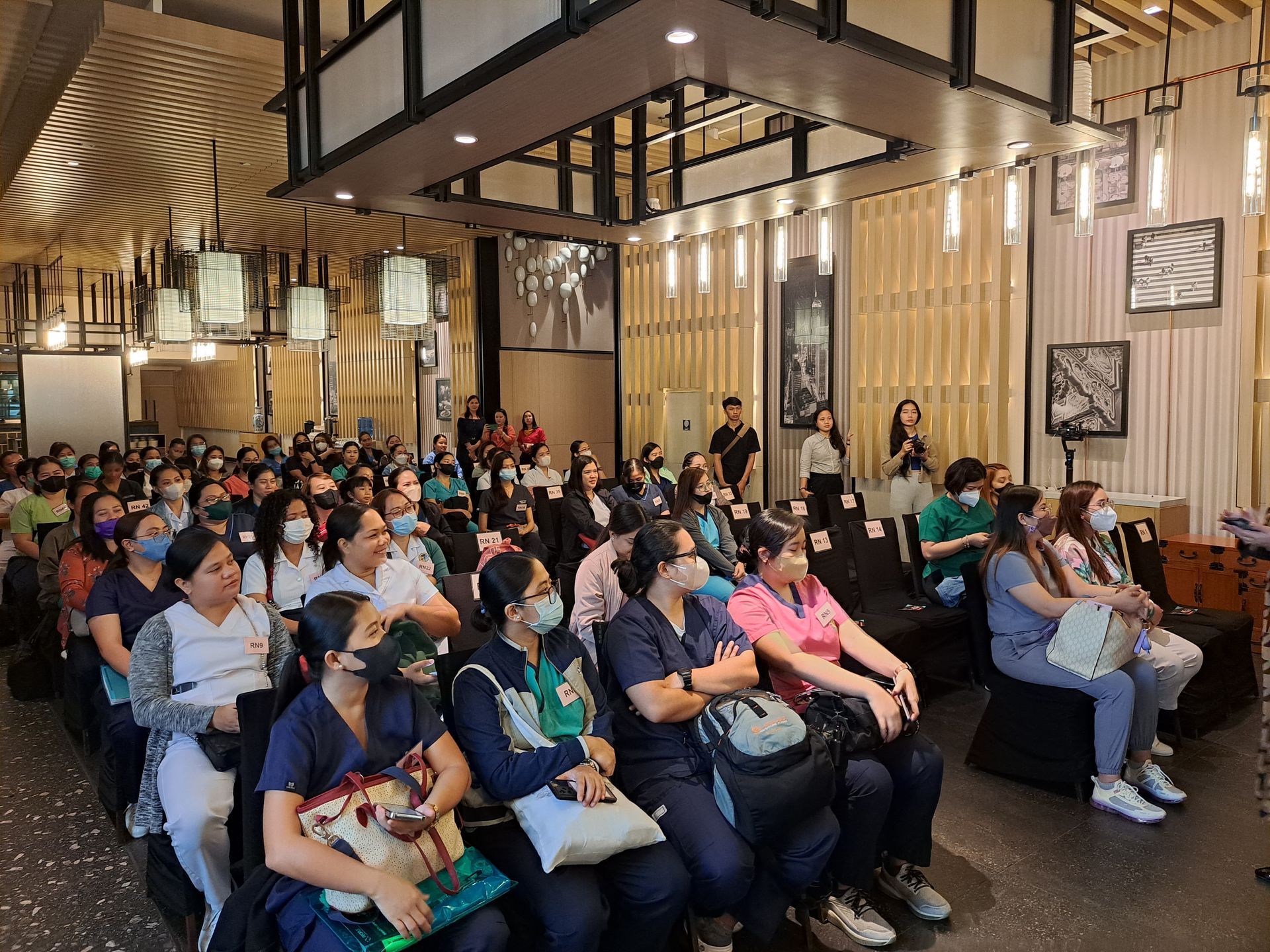 A large group of people are sitting in a room wearing masks.