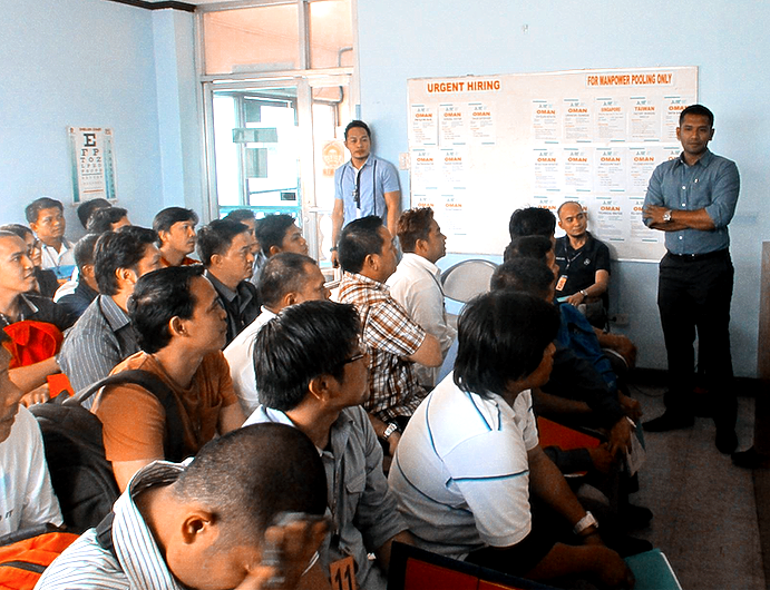 A group of people are sitting in a room with a man standing in front of them
