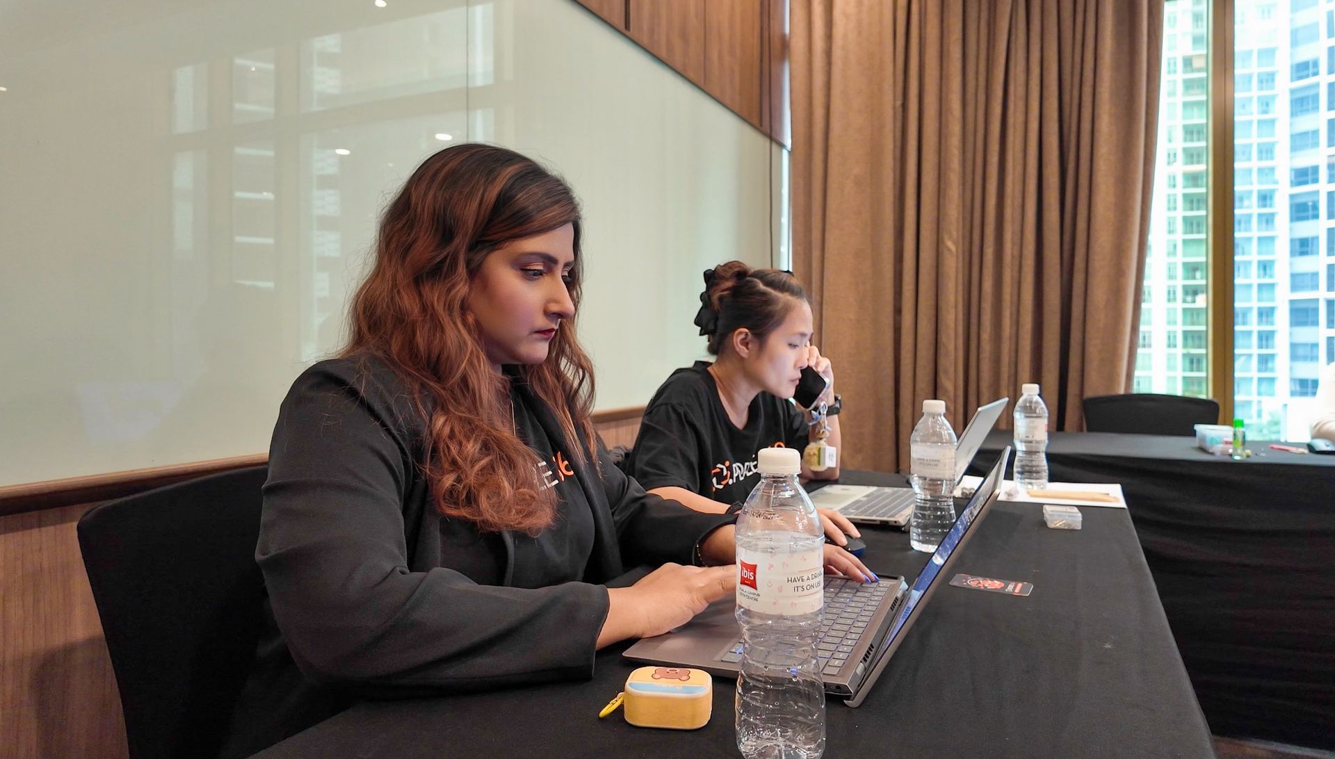 Two women are sitting at a table using laptops.