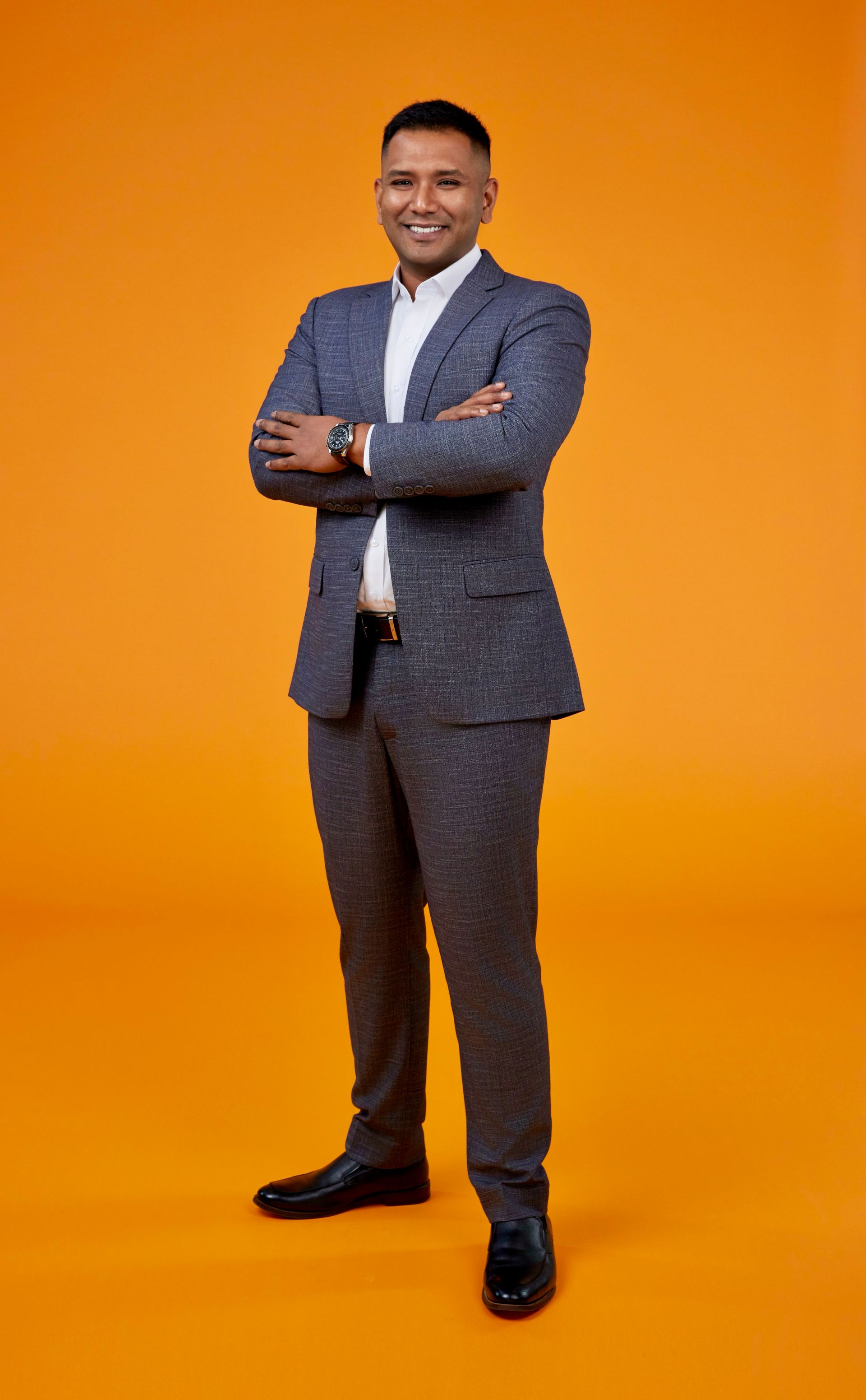 A man in a suit is standing with his arms crossed on an orange background.