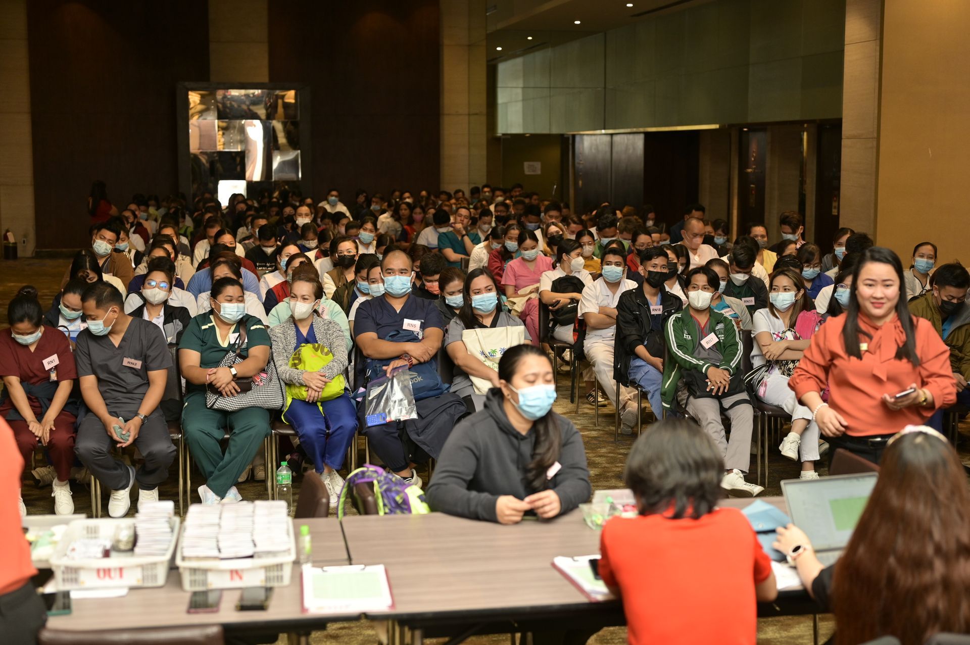 A large group of people wearing masks are sitting at tables in a room.