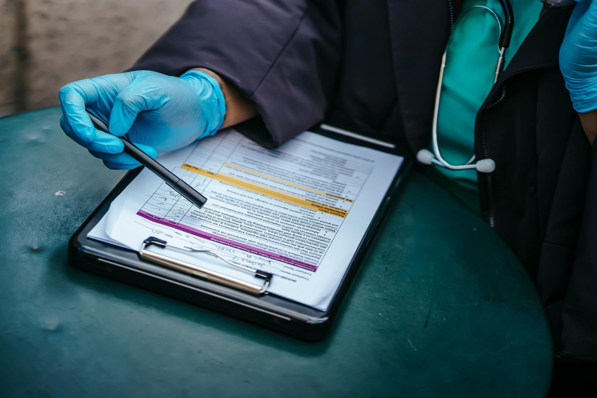A doctor wearing blue gloves is writing on a clipboard with a pen.