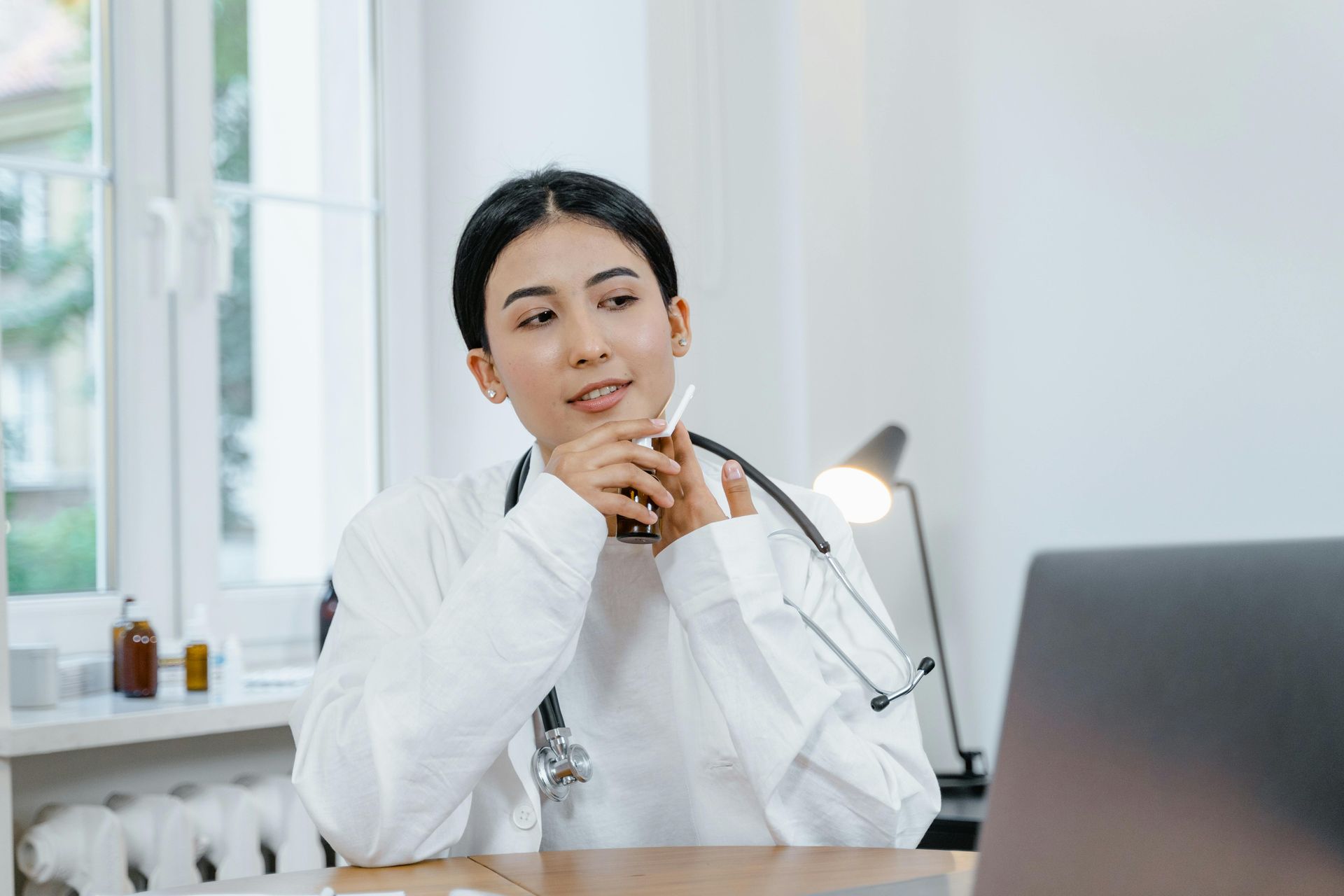 A female doctor is sitting at a desk in front of a laptop computer.