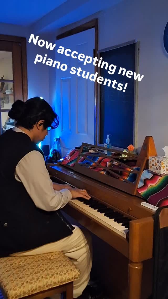 A woman is sitting on a stool playing a piano.