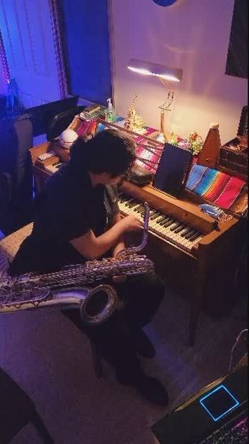 A man is sitting at a piano playing a saxophone.