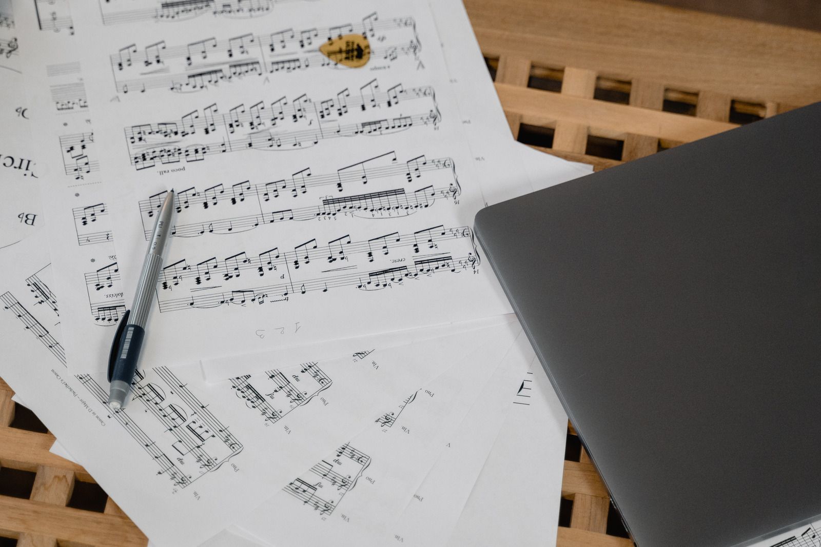 A pen is sitting on top of a pile of sheet music next to a laptop.