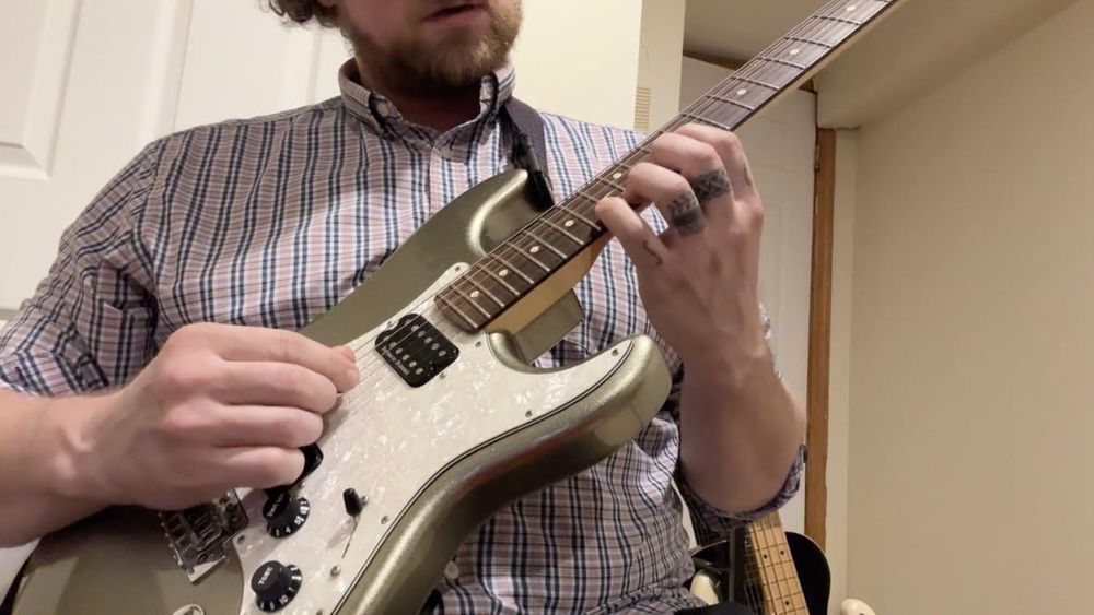 A man in a plaid shirt is playing an electric guitar.