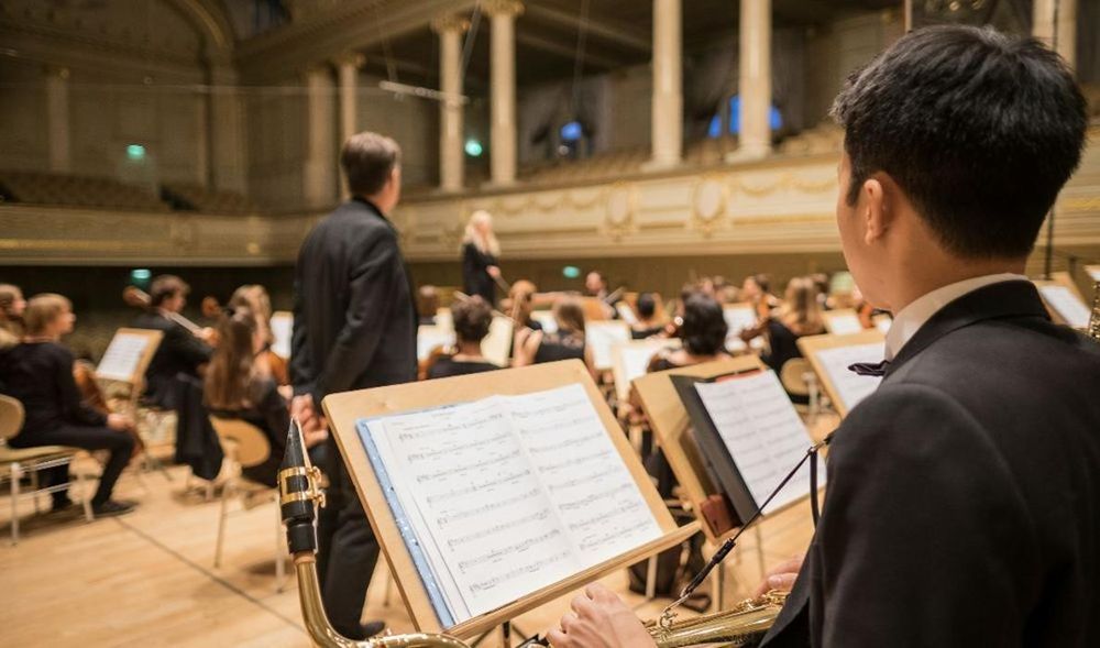 A man is playing a saxophone in front of an orchestra.