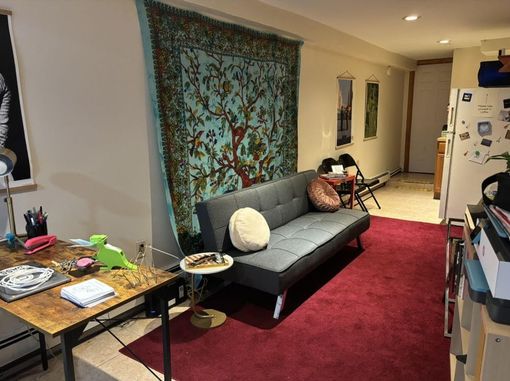 A living room with a couch , table , chairs and a tapestry on the wall.