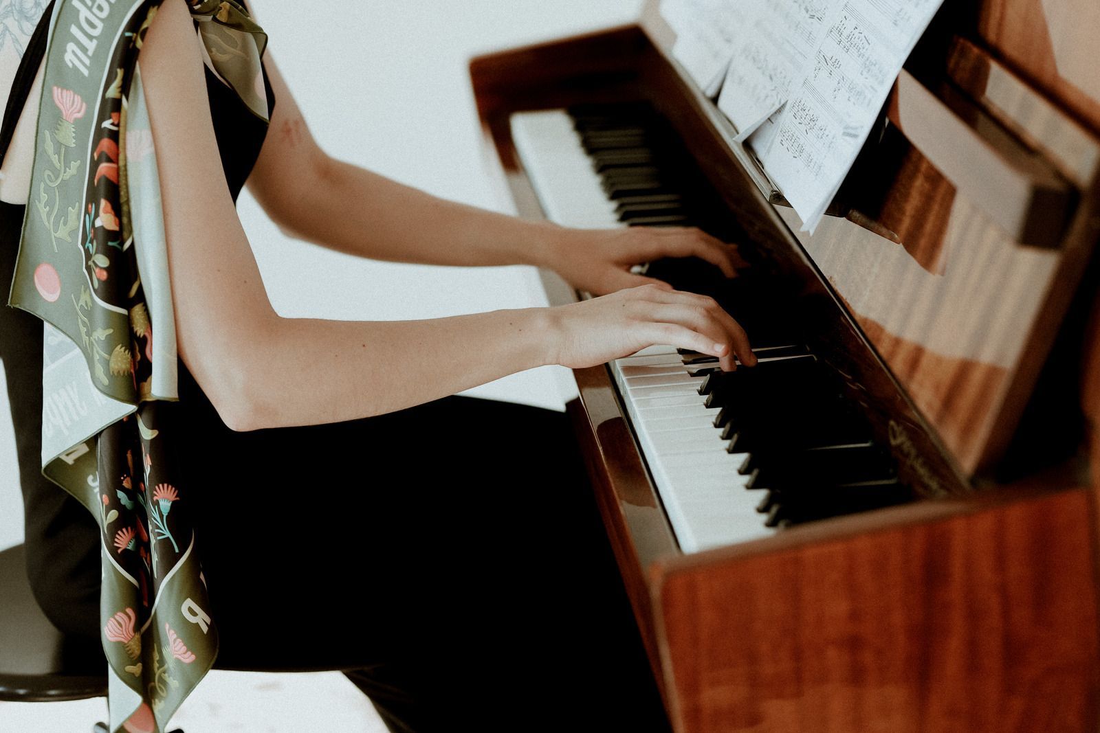 Person playing a wooden upright piano beside sheet music