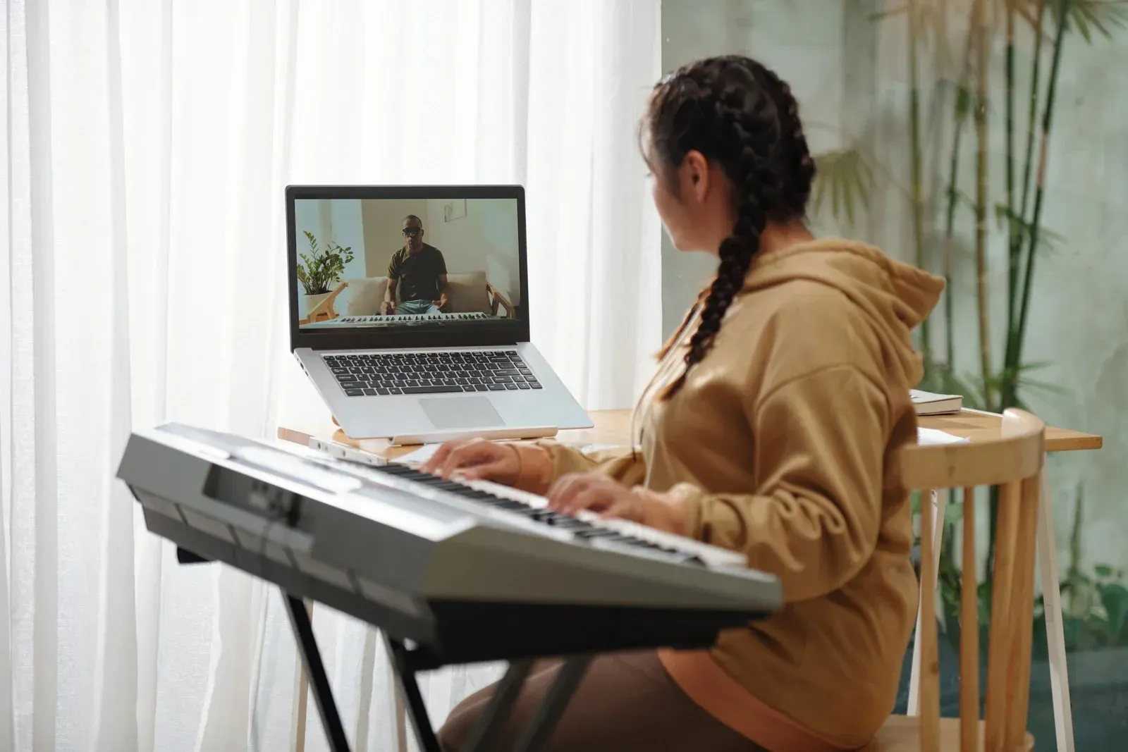 Person playing a keyboard while video chatting on a laptop in a bright home room