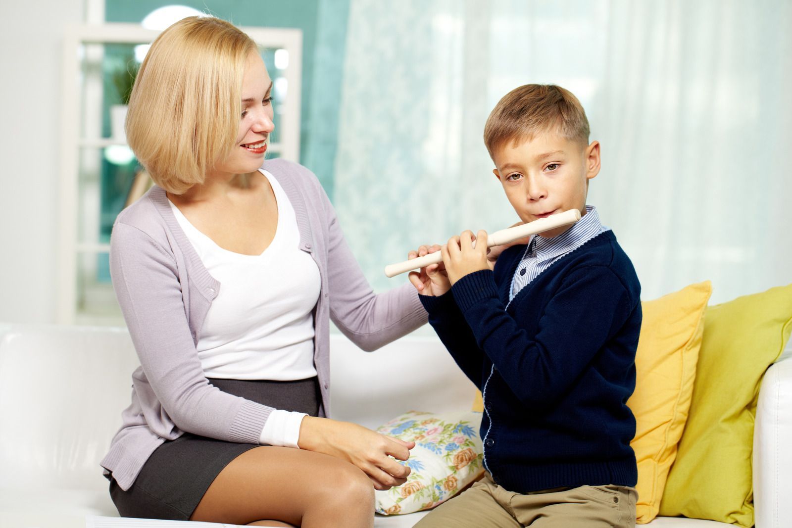 A woman is teaching a boy how to play a flute.