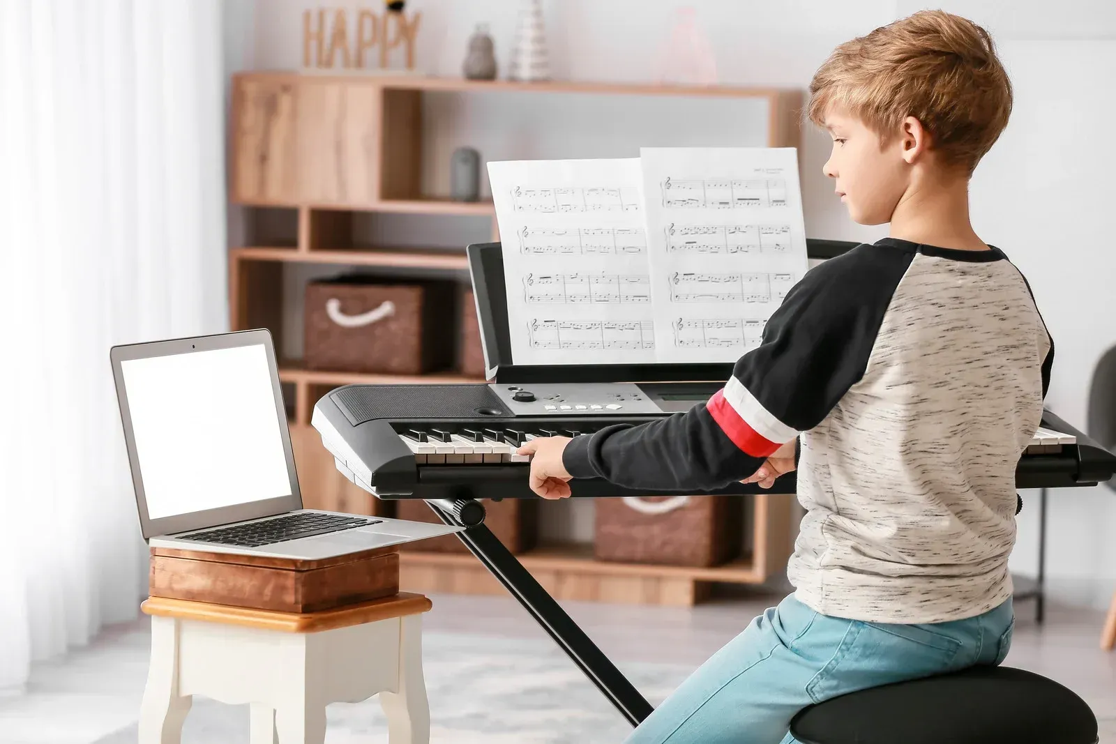 A young boy is sitting at a keyboard in front of a laptop computer.