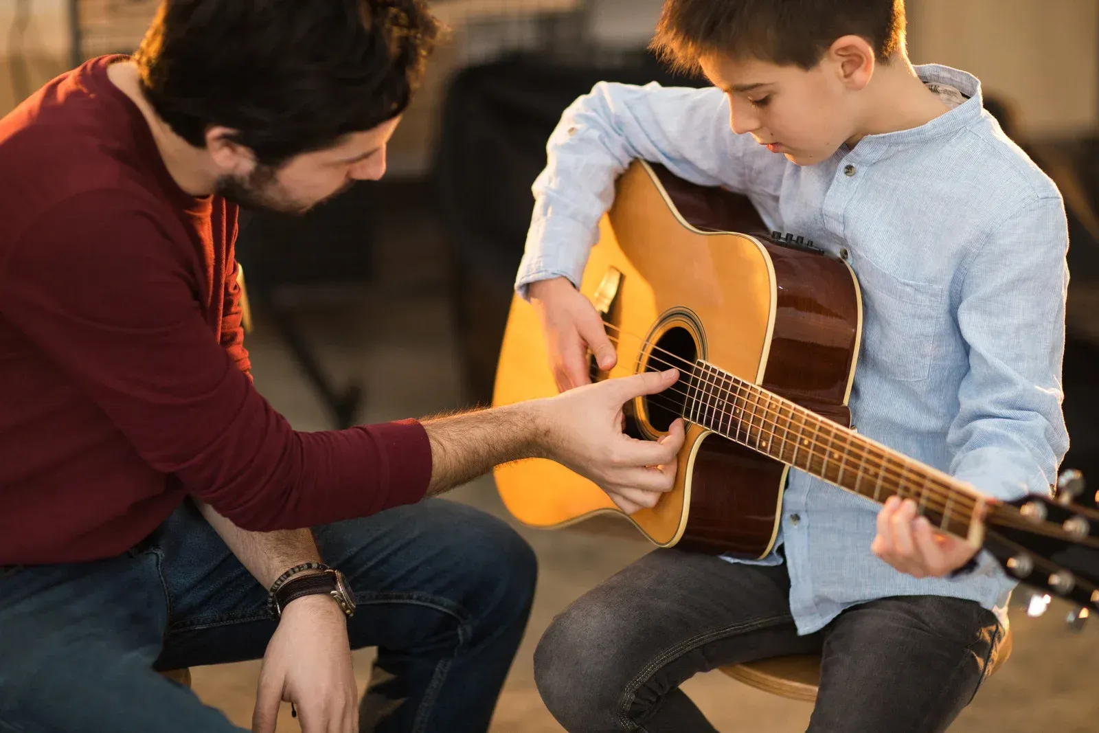 A man is teaching a young boy how to play an acoustic guitar.