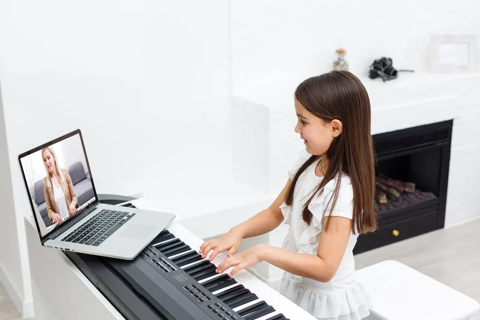 A little girl is playing a piano in front of a laptop computer.