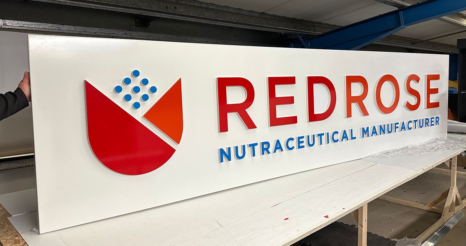 Sign for Red Rose Nutraceutical Manufacturers: white background with red and blue logo and text.