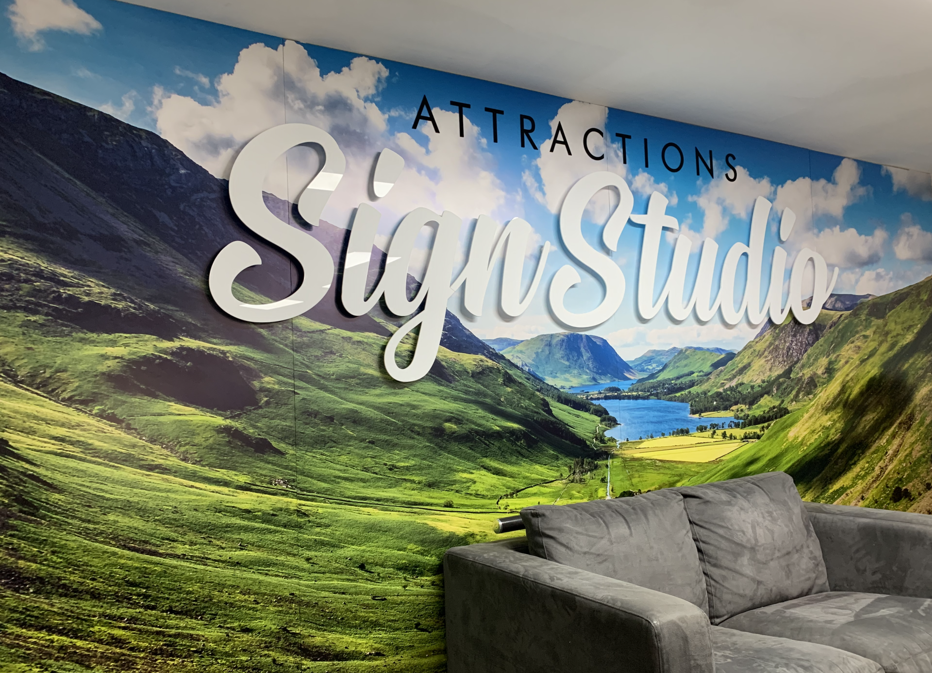 Sign Studio logo on a wall mural of a scenic mountain landscape next to a grey sofa.