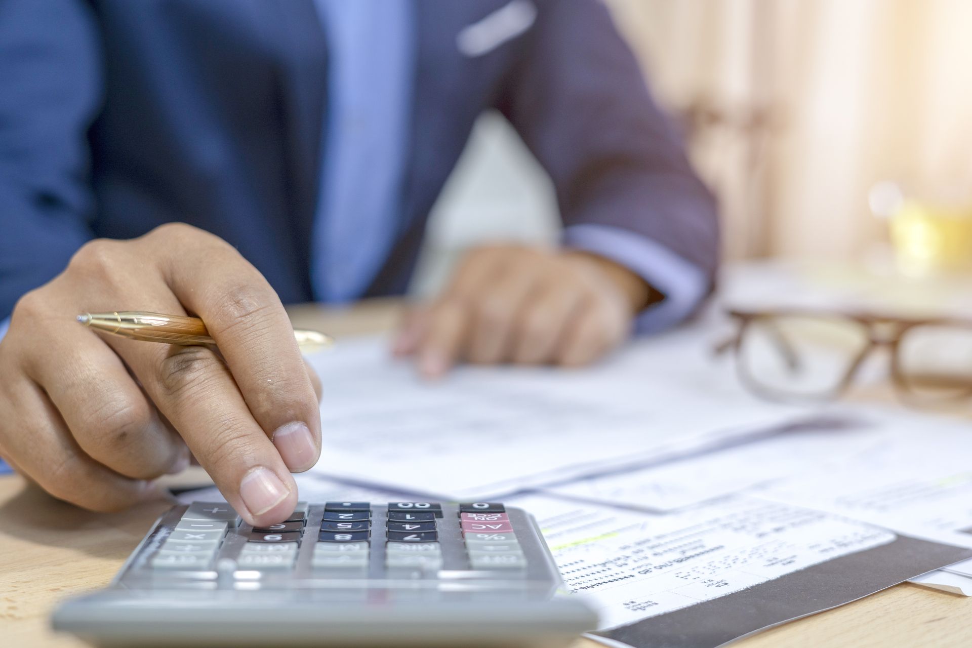 Person in a suit using a calculator on a desk, reviewing documents.