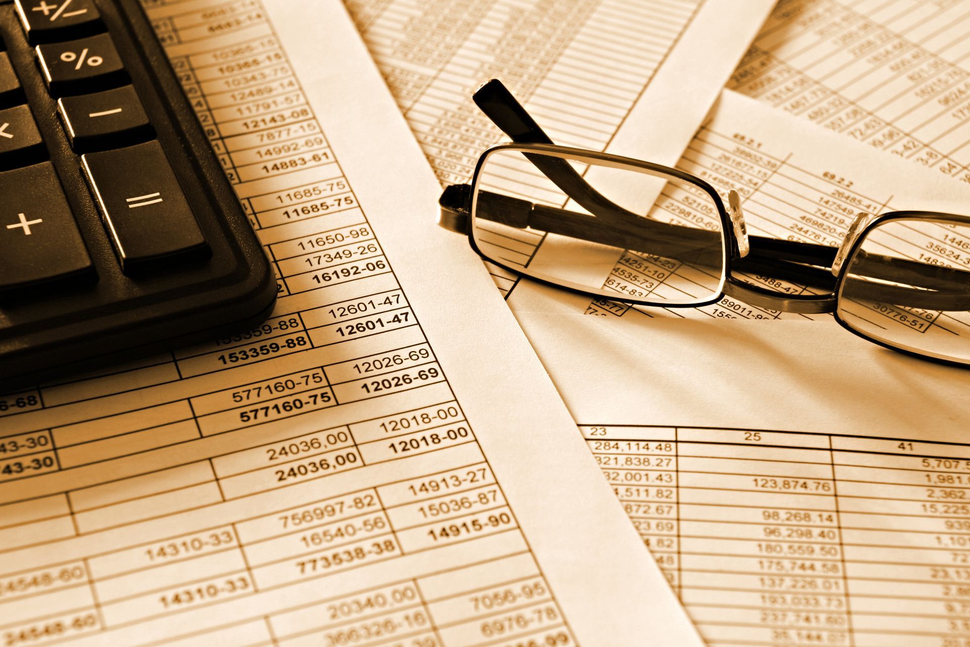 Calculator and eyeglasses rest on financial documents with numerical data.