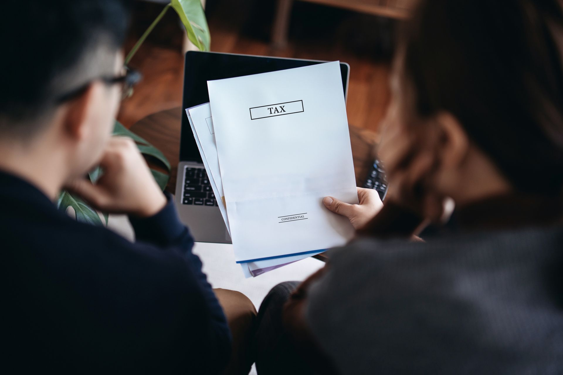Two people reviewing documents, one holding a contract. Laptop and plant visible.