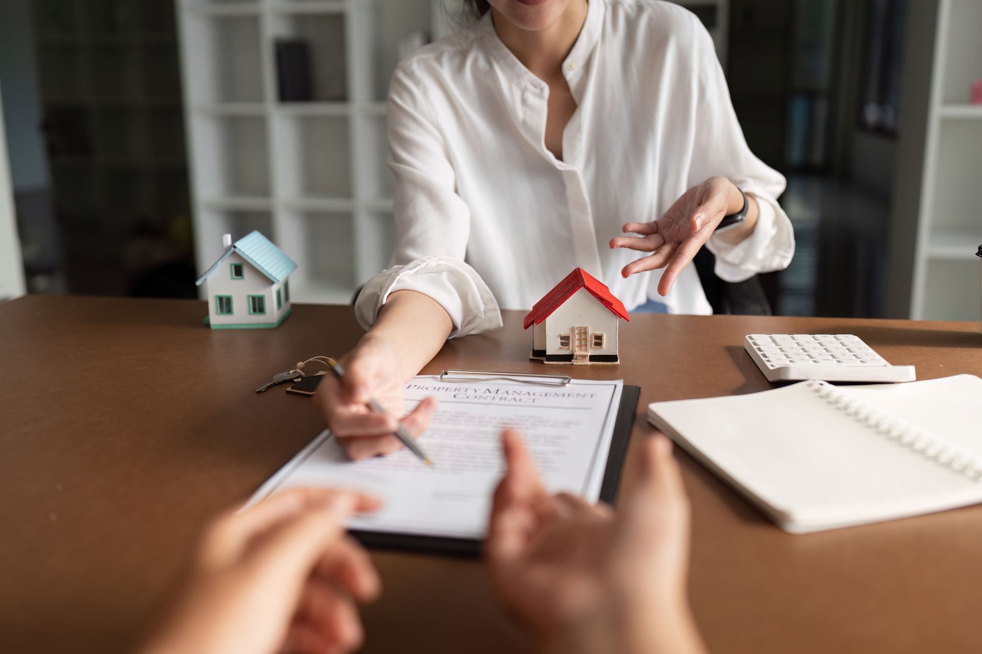 Real estate agent explaining contract terms to a client, with house models and keys on the desk.