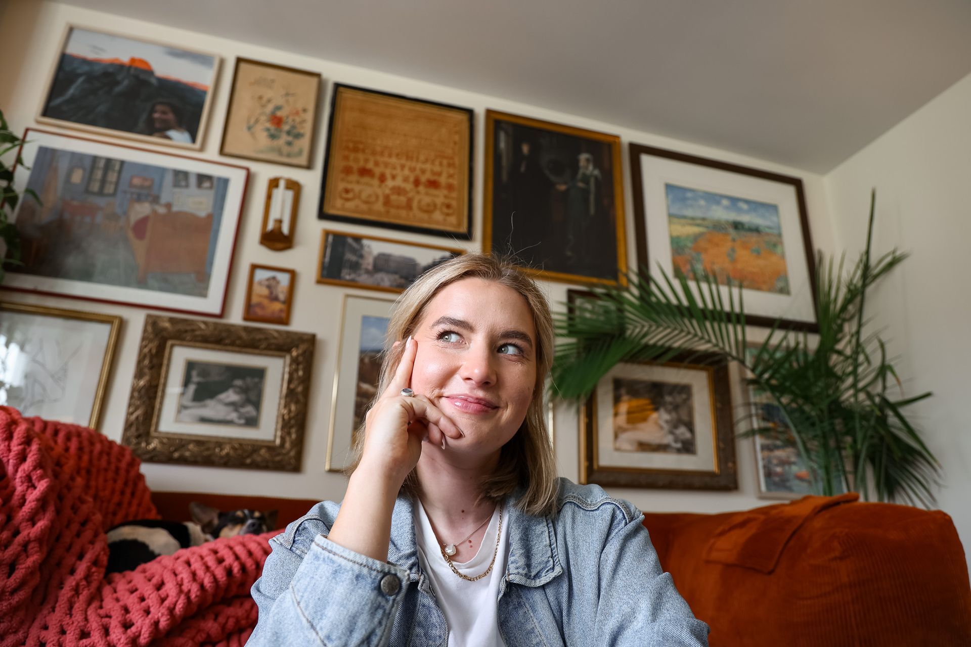A person sits in front of a gallery wall with framed art, resting their chin on their hand with a thoughtful expression.