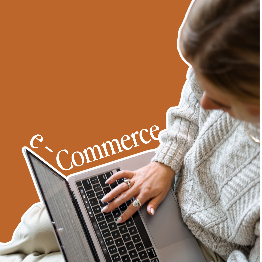 Person in a sweater types on a laptop, sitting on a couch with a rug nearby.