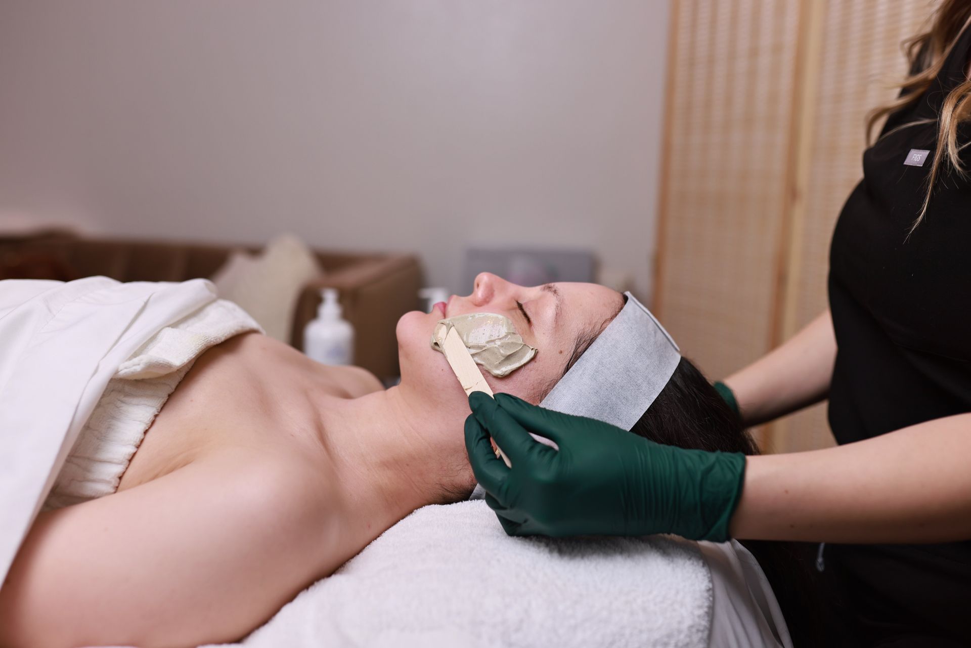 Facial treatment: A person's face is covered in a mask while a gloved hand applies a strip in a spa.