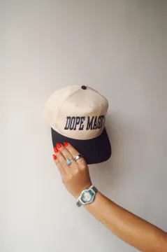 A person’s hand holds up a beige and black baseball cap with 