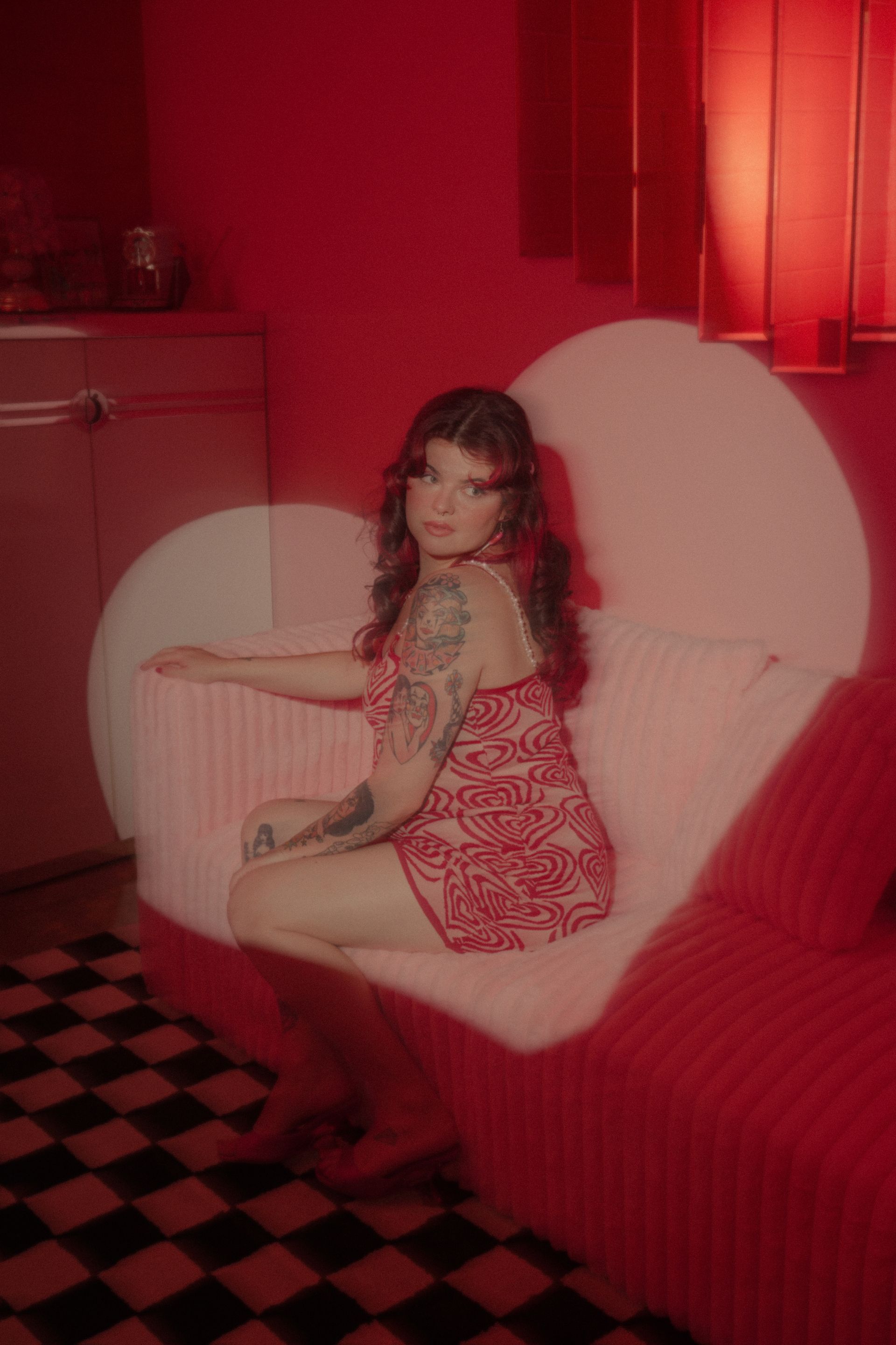 Woman in red dress on a heart-shaped couch, red room.