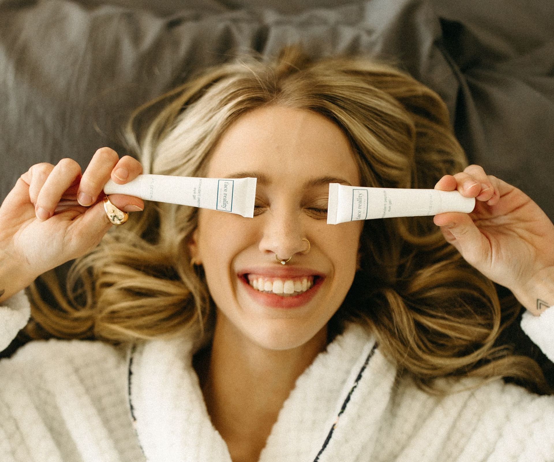 A woman is laying on a bed holding two tubes in front of her eyes.