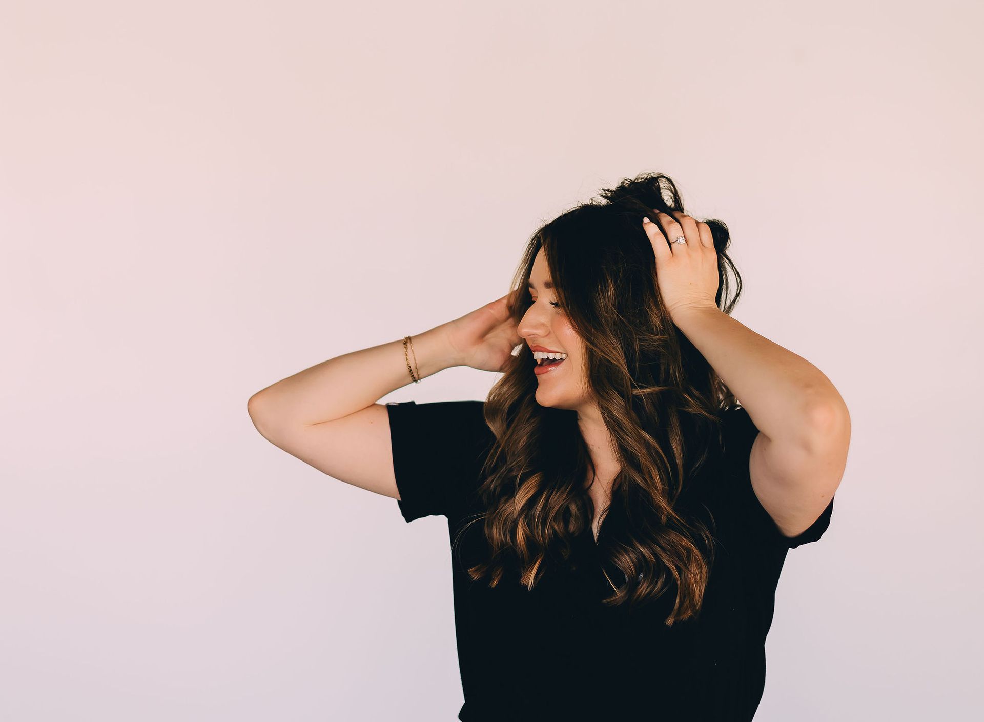 A woman in a black shirt is holding her hair in her hands.