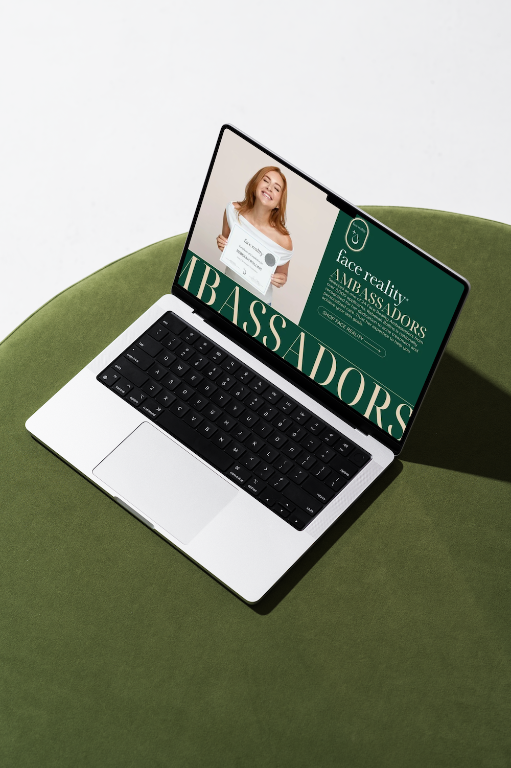 A laptop displays a graphic with the word AMBASSADORS and a person holding a sign, sitting on a round green surface.