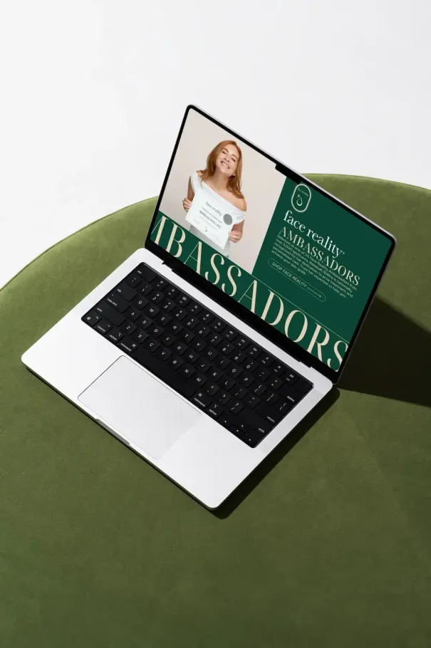 A laptop displays a graphic with the word AMBASSADORS and a person holding a sign, sitting on a round green surface.
