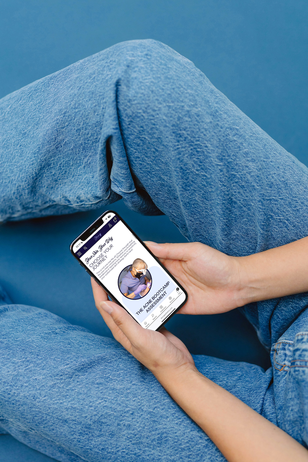 A person in blue jeans holds a smartphone displaying a social media profile with an avatar against a blue background.