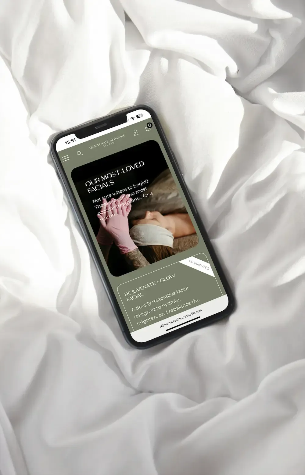 A smartphone resting on white, rumpled fabric displays a webpage about skincare with a photo of a facial treatment.