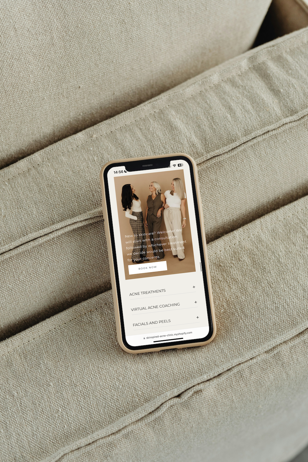 A smartphone resting on a beige fabric couch displays a retail website with a photo of three people.