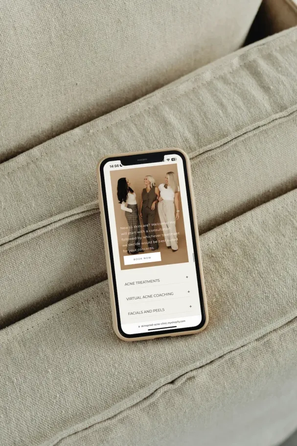 A smartphone resting on a beige fabric couch displays a retail website with a photo of three people.