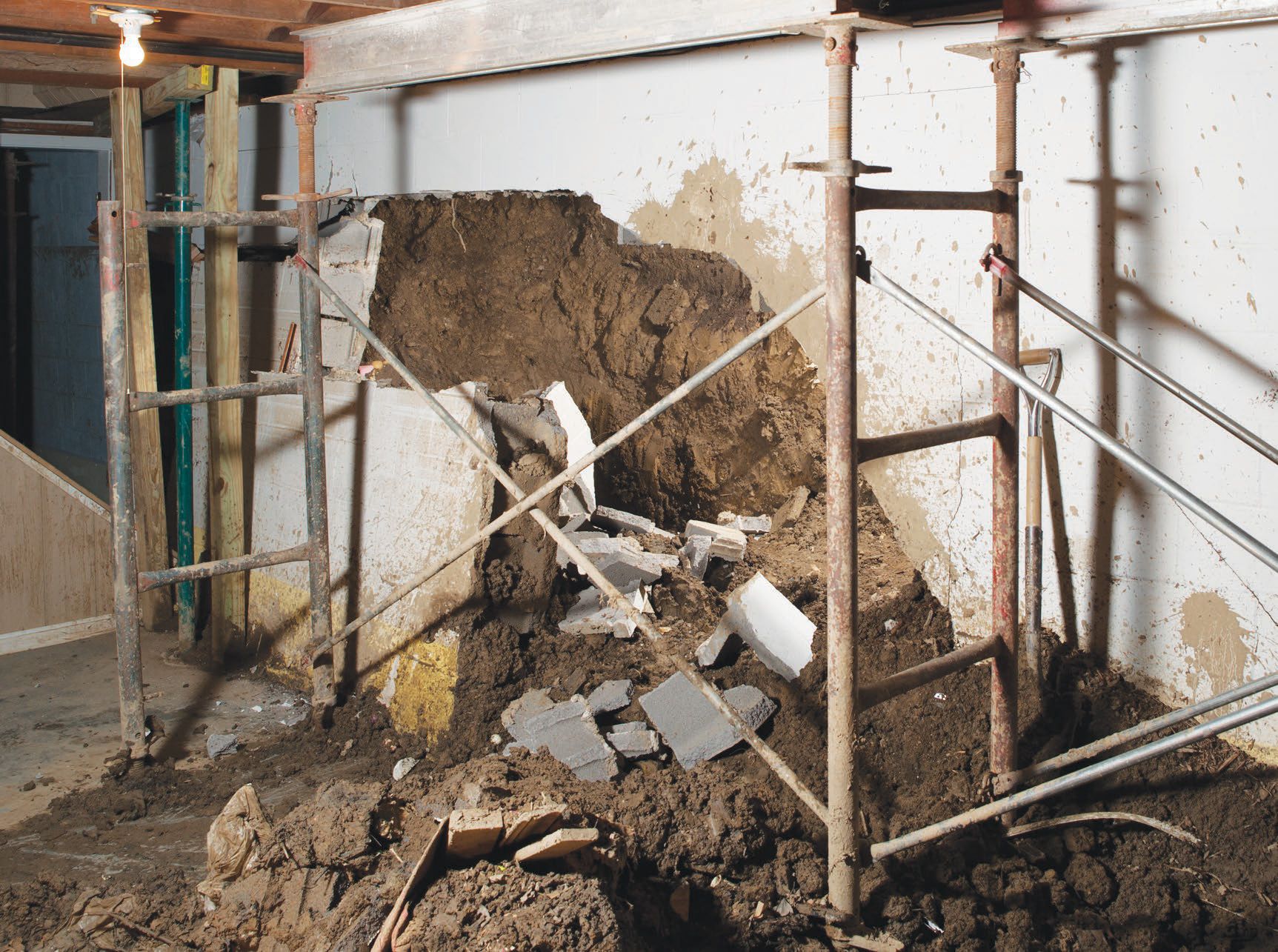 Wall partially collapsed, supported by metal scaffolding, debris on floor.