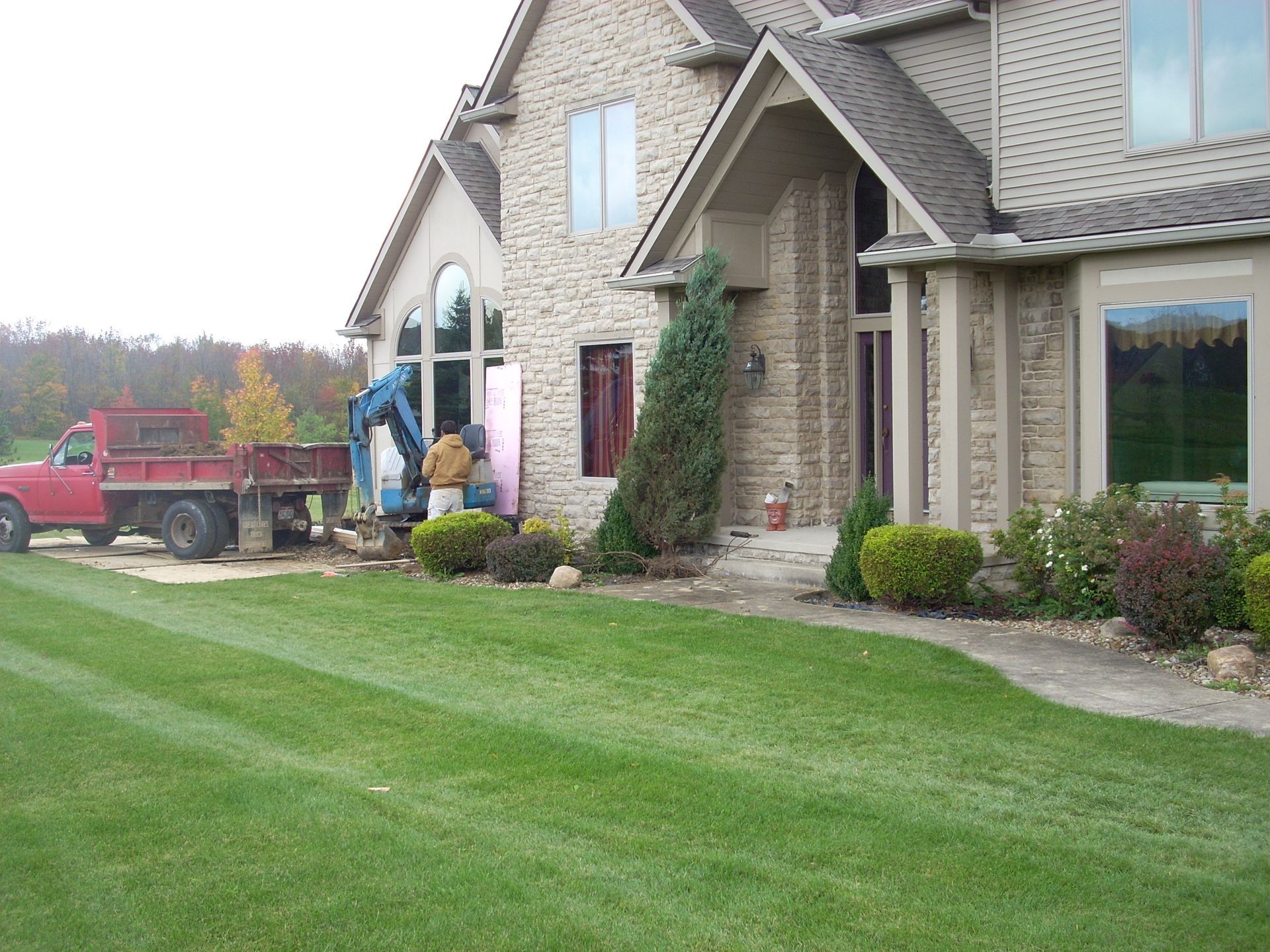 Workers beside a brick home unloading materials from a red truck on a lawn.