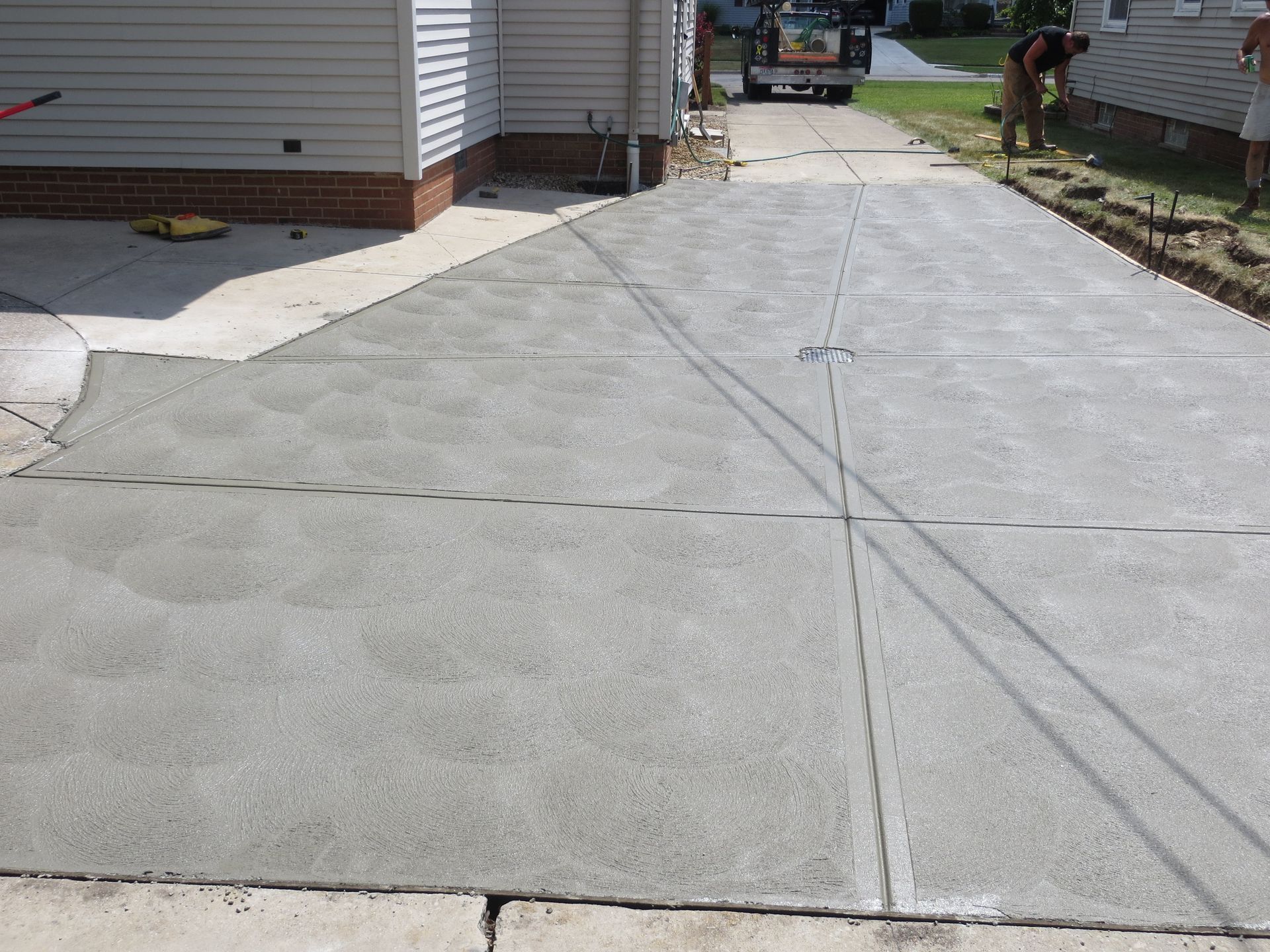 Freshly poured concrete driveway, next to a house, with workers in the background.