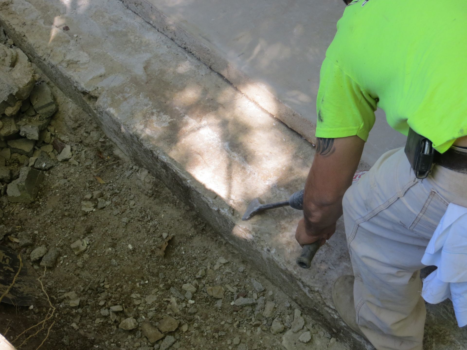 Person in neon green shirt working on concrete, using a tool. Dirt and partially finished concrete.