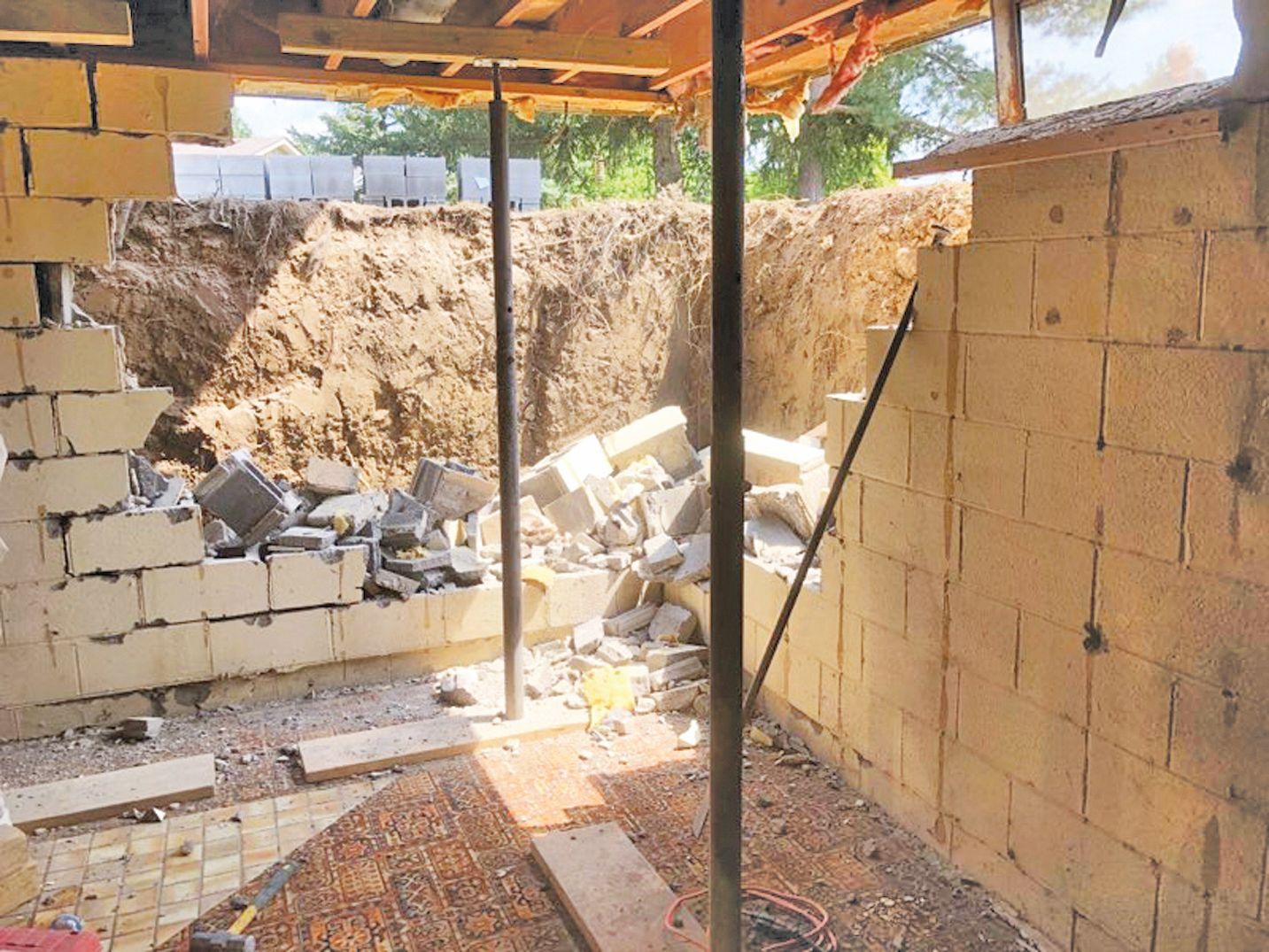 Construction site with a partially demolished block wall supported by metal poles.