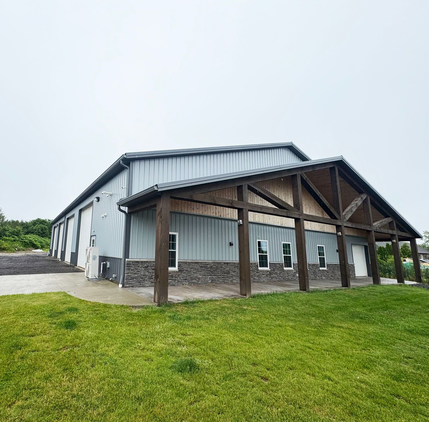 A large metal building with a wooden porch, set on a grassy area under a gray sky.