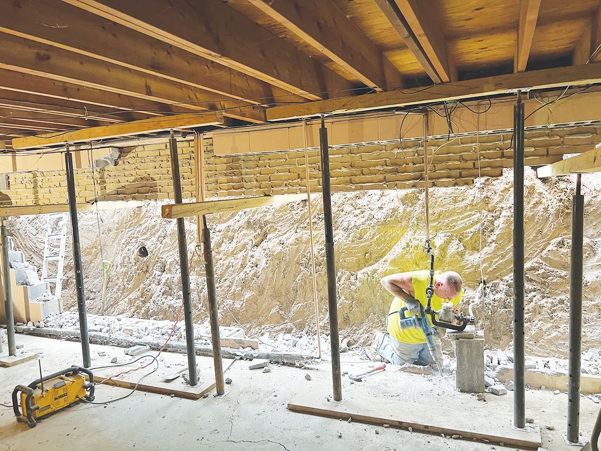 A construction worker uses a tool to work on a foundation supported by temporary steel columns.