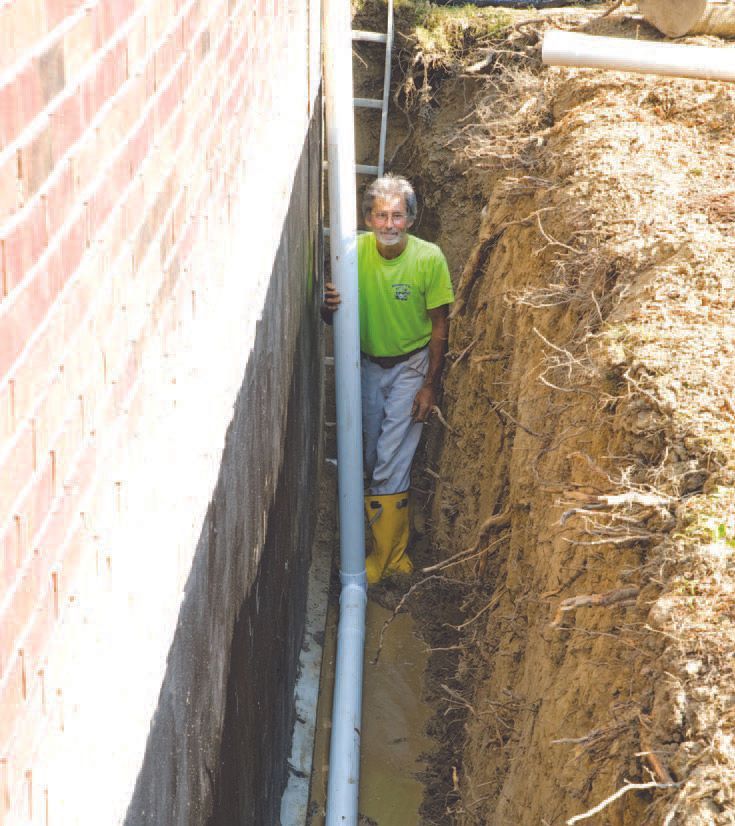Man in trench holding pipe next to a brick wall. Earth walls on the right.