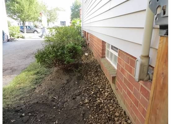 Exterior of a brick and white-sided building with gravel bed. Green bushes grow along the wall near a driveway.