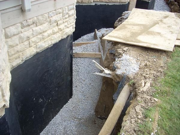 Foundation waterproofing work with gravel, drainage pipe, and black membrane.