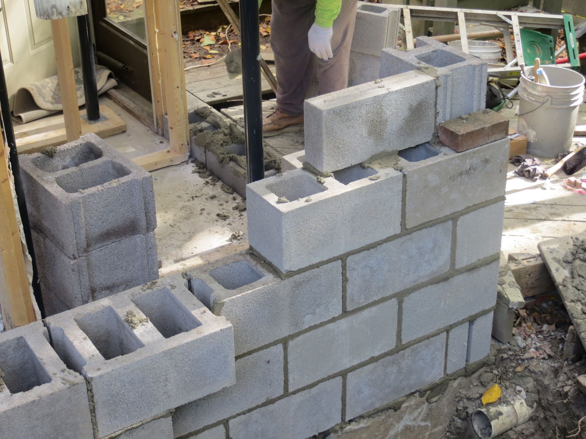 Person laying concrete blocks to build a wall outdoors.