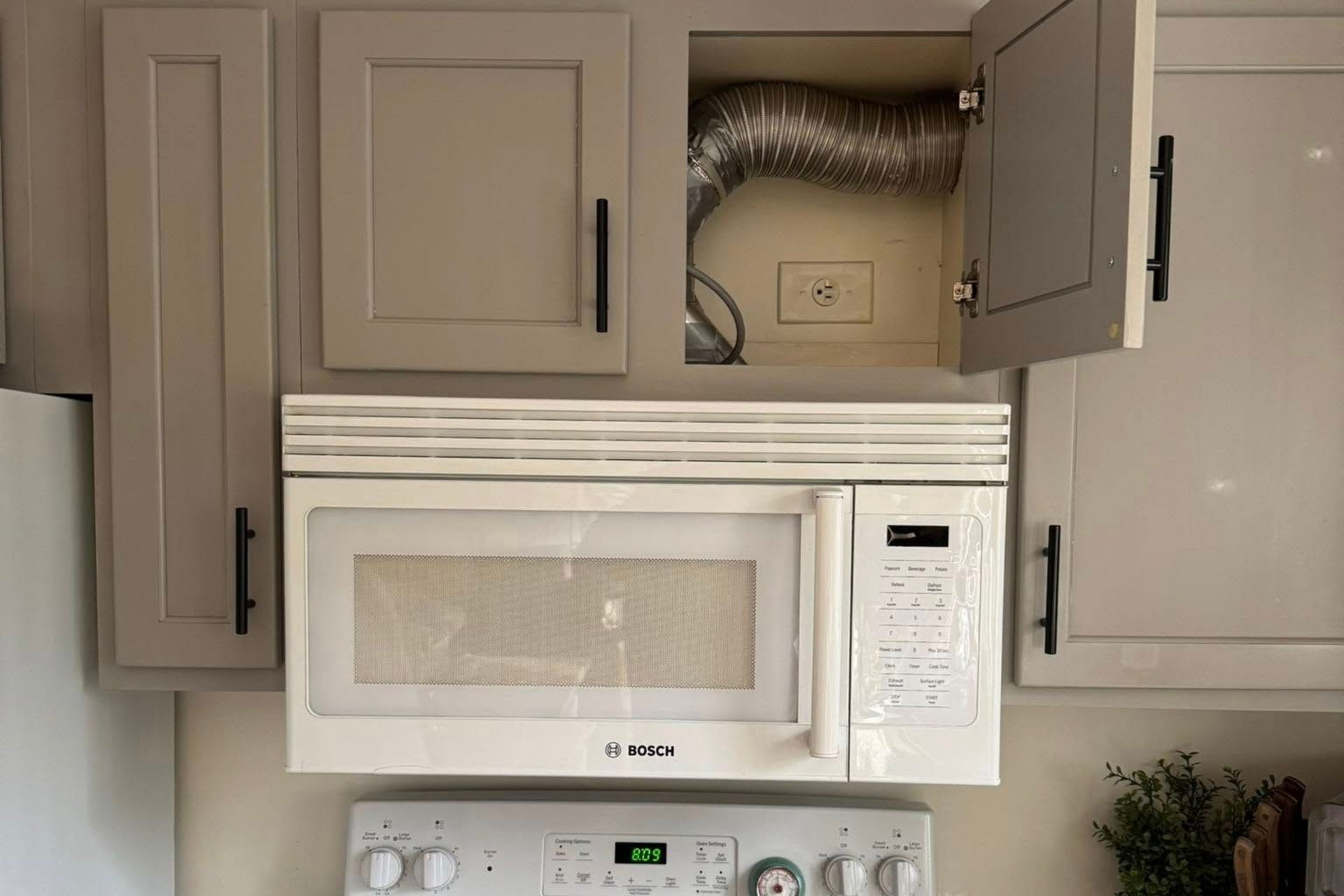 Kitchen cabinets, microwave over a stove, and an open cabinet revealing a vent.